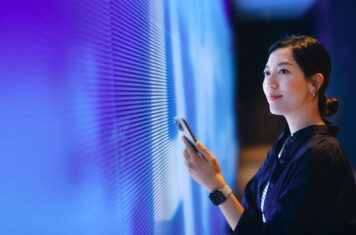 Woman with phone facing large video screen