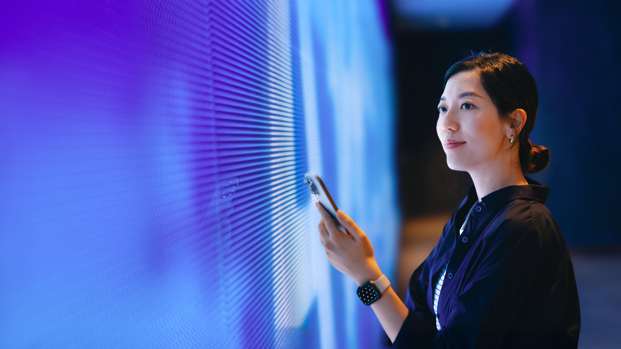 Woman with phone facing large video screen