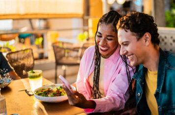 Happy woman and man leaving review on phone in a restaurant