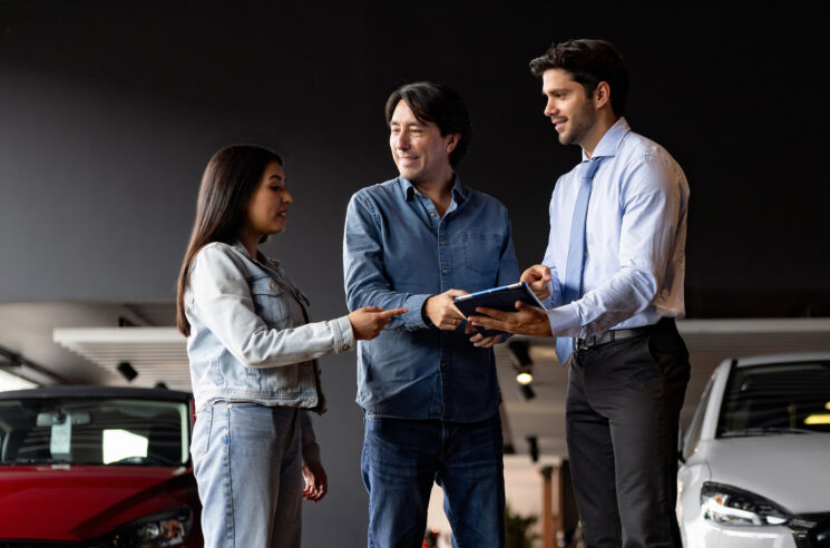 Customers working with auto salesman in showroom.
