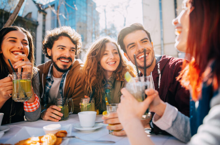 Group of young adults enjoying drinks at an outdoor table.