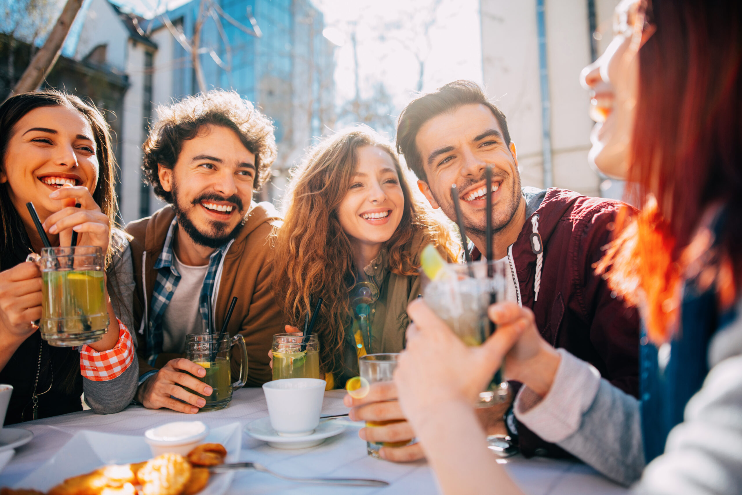 Group of young adults enjoying drinks at an outdoor table.
